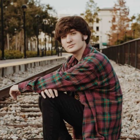 Dean Keeley looking at the camera, sitting next to railroad tracks.